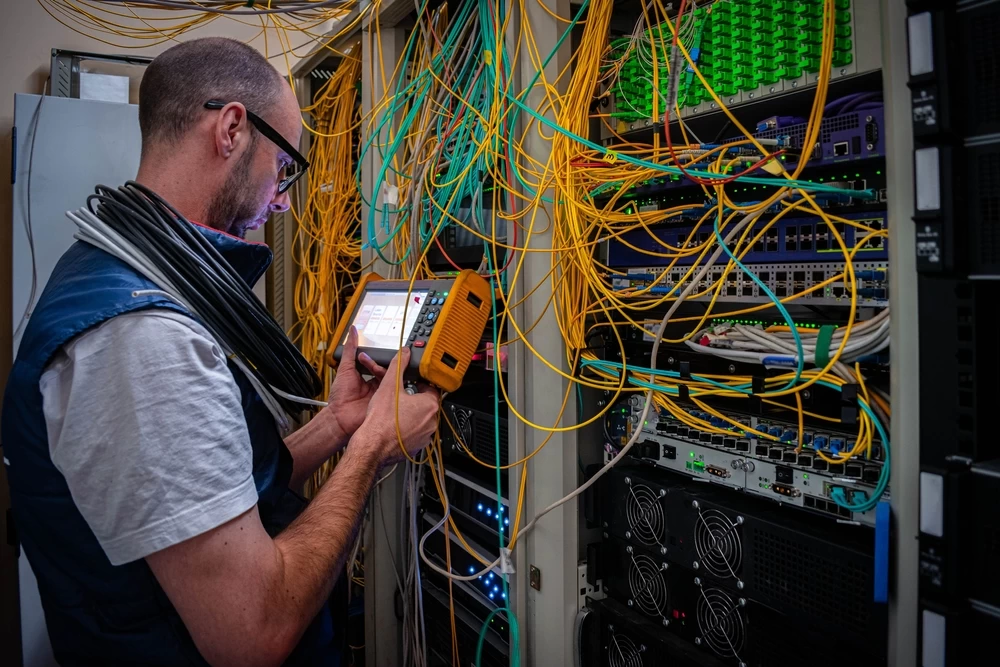 Technician testing fiber connections in a network rack